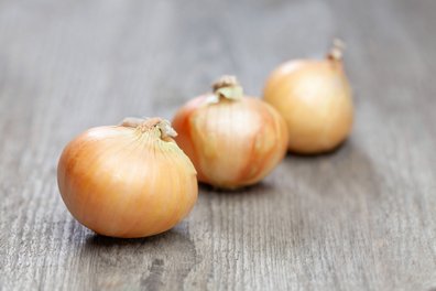 Drei Zwiebeln liegen auf einem Holztisch