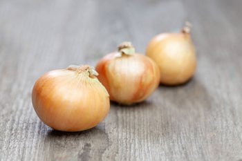 Drei Zwiebeln liegen auf einem Holztisch