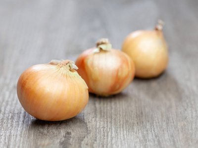 Drei Zwiebeln liegen auf einem Holztisch