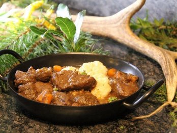 Hirschragout in kleiner Pfanne gekocht mit Hirschgeweih im Hintergrund