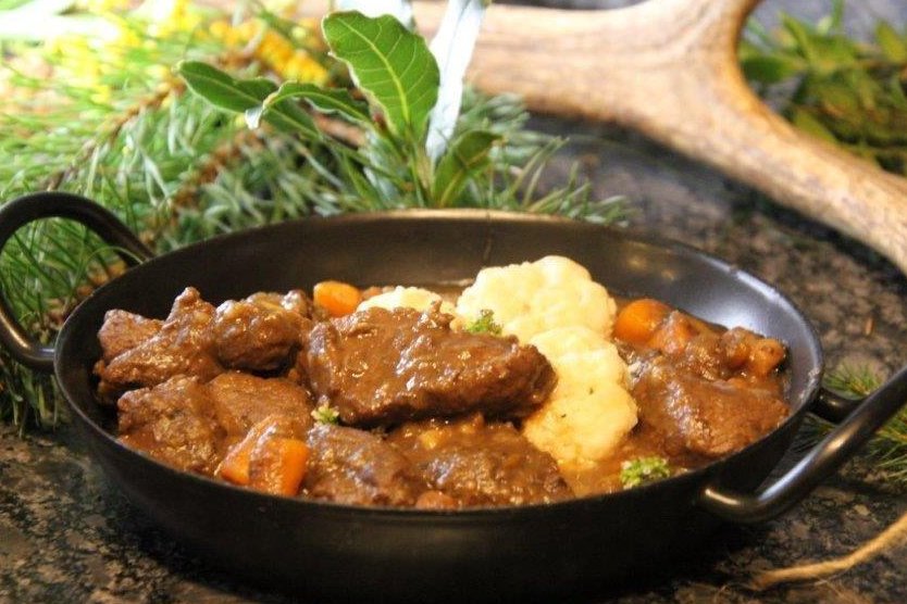 Hirschragout in kleiner Pfanne gekocht mit Hirschgeweih im Hintergrund