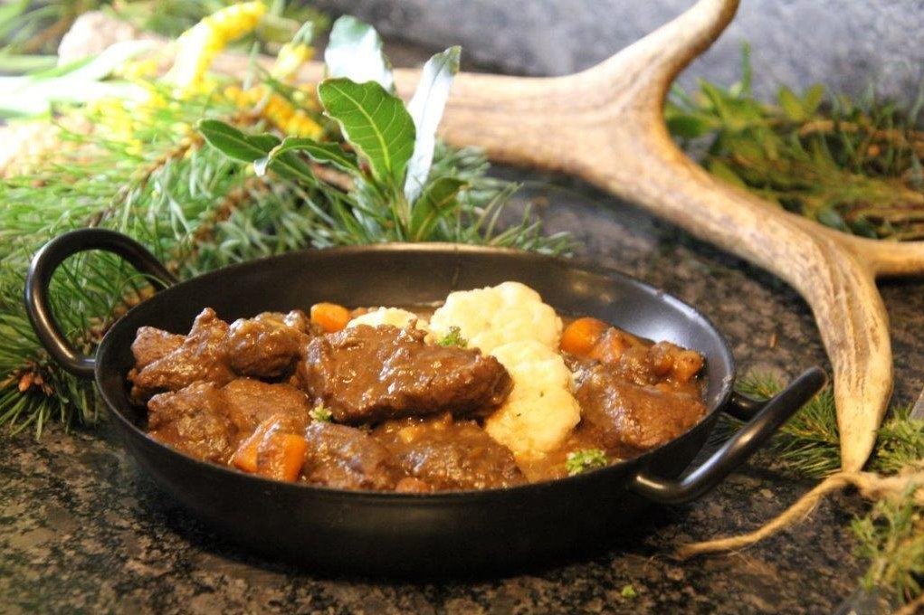 Hirschragout in kleiner Pfanne gekocht mit Hirschgeweih im Hintergrund