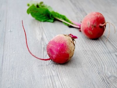 Zwei Rote Rüben mit Blättern auf einem Holztisch