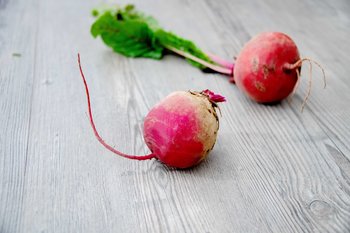 Zwei Rote Rüben mit Blättern auf einem Holztisch