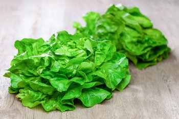 Zwei Salatköpfe liegen auf einem Holztisch