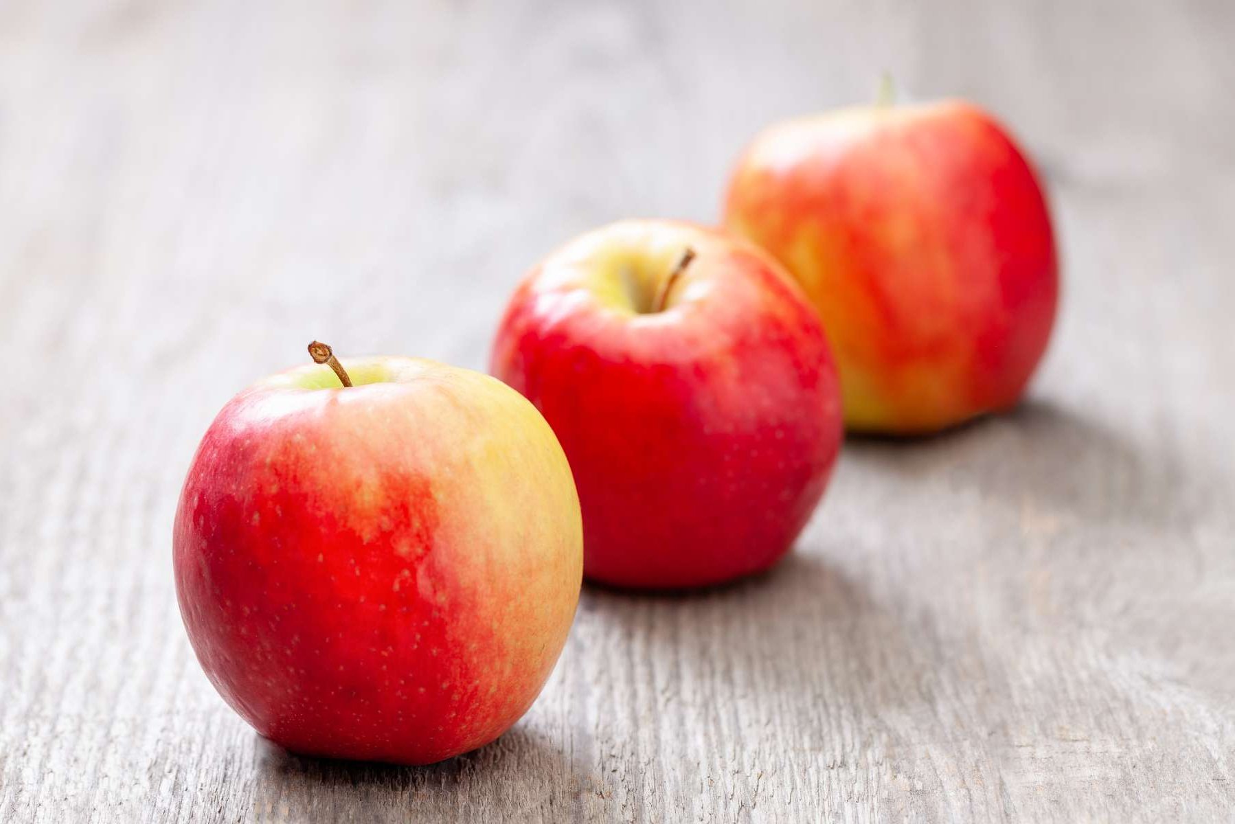 Drei Äpfel liegen auf einem Holztisch