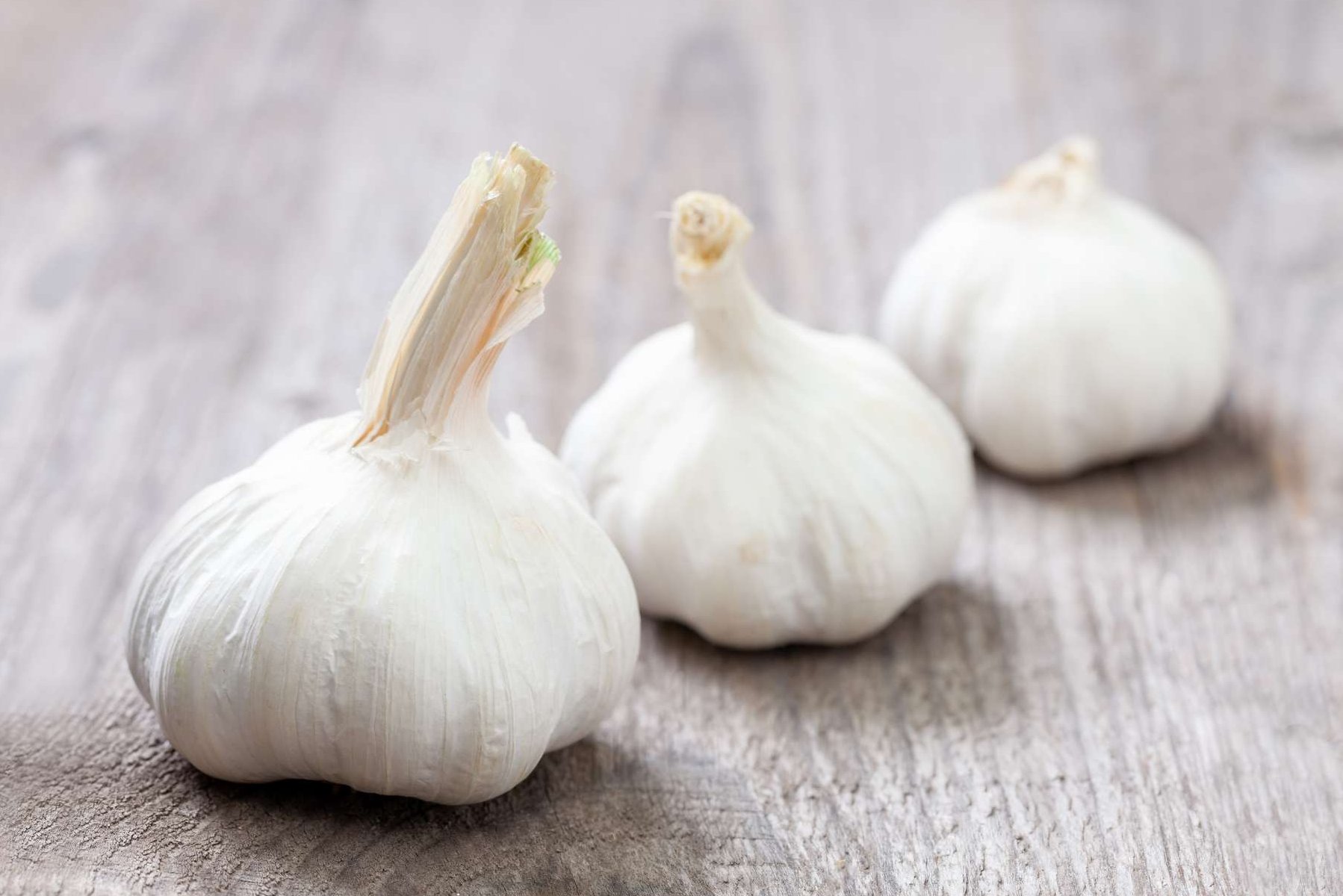 Drei Knoblauchzwiebeln liegen auf einem Holztisch