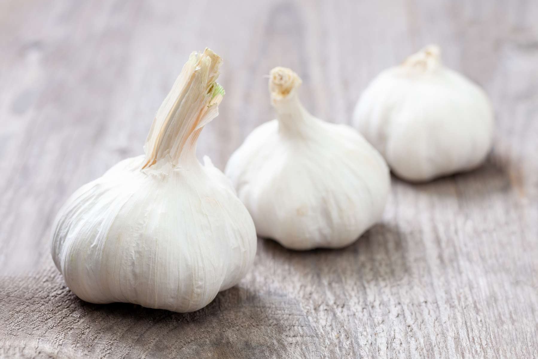Drei Knoblauchzwiebeln liegen auf einem Holztisch