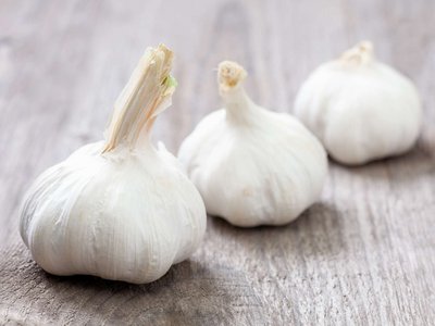 Drei Knoblauchzwiebeln liegen auf einem Holztisch