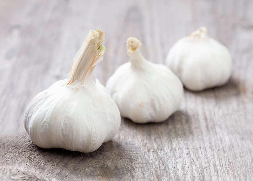 Drei Knoblauchzwiebeln liegen auf einem Holztisch