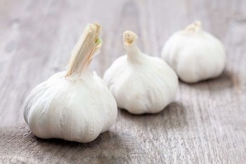 Drei Knoblauchzwiebeln liegen auf einem Holztisch