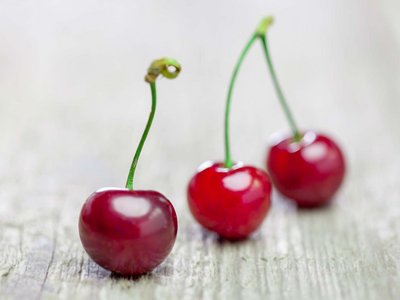 Drei Kirschen liegen auf einem Holztisch