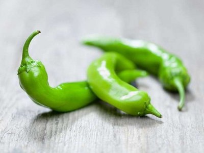 Drei grüne Pfefferoni liegen auf einem Holztisch