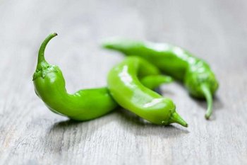 Drei grüne Pfefferoni liegen auf einem Holztisch