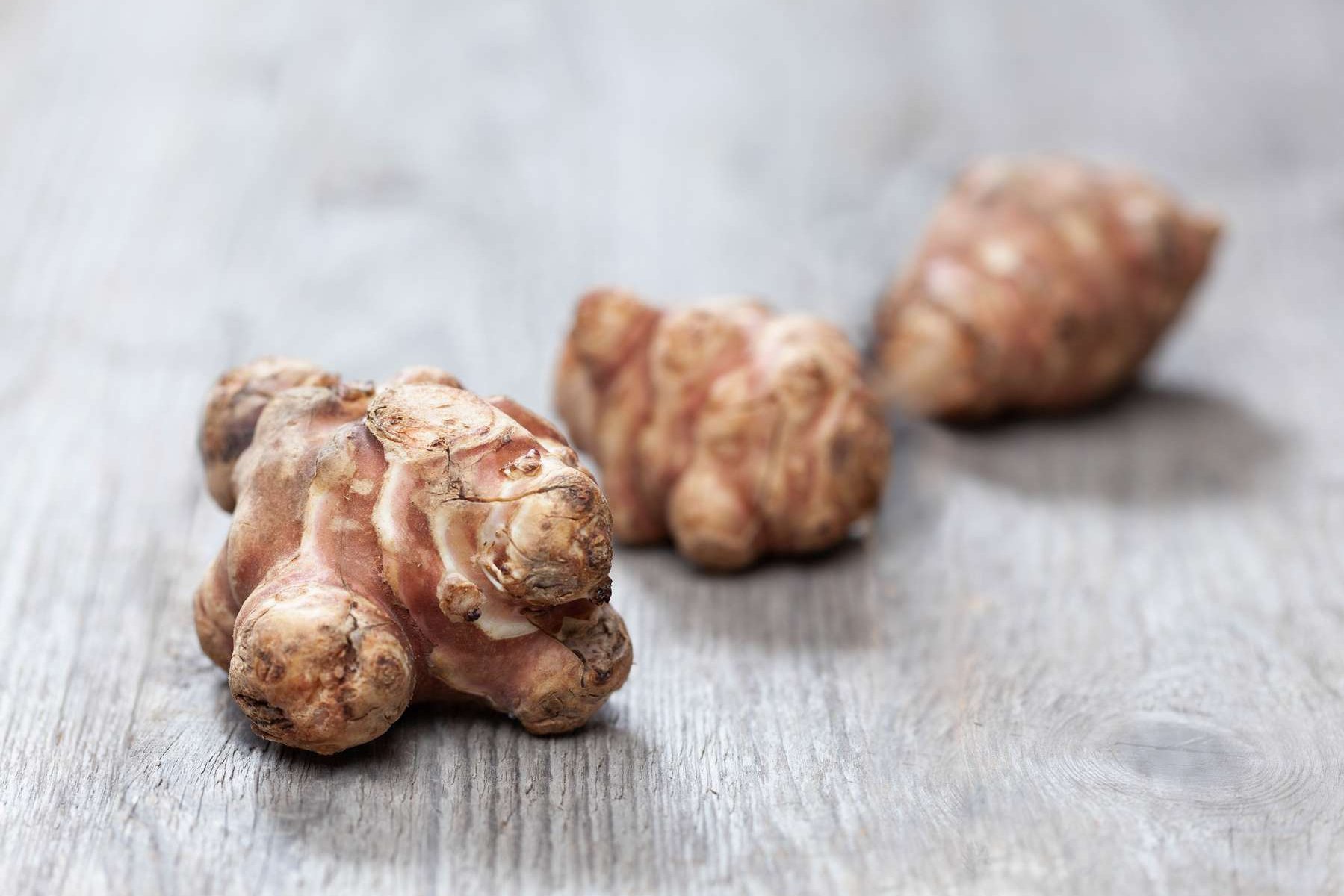 Drei Knollen Topinambur liegen auf einem Holztisch