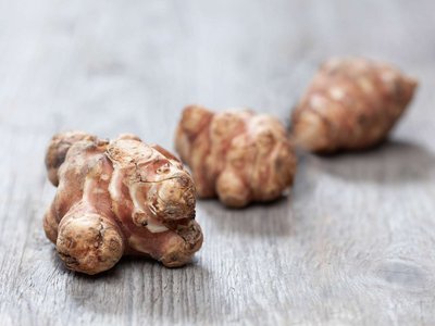 Drei Knollen Topinambur liegen auf einem Holztisch