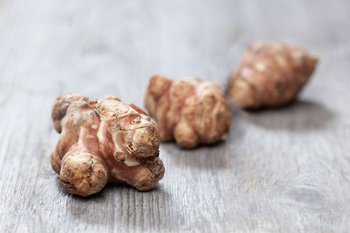 Drei Knollen Topinambur liegen auf einem Holztisch