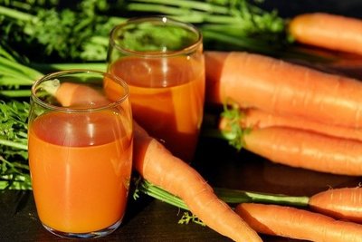 Zwischen liegenden Karotten stehen zwei Gläser mit Karottensaft