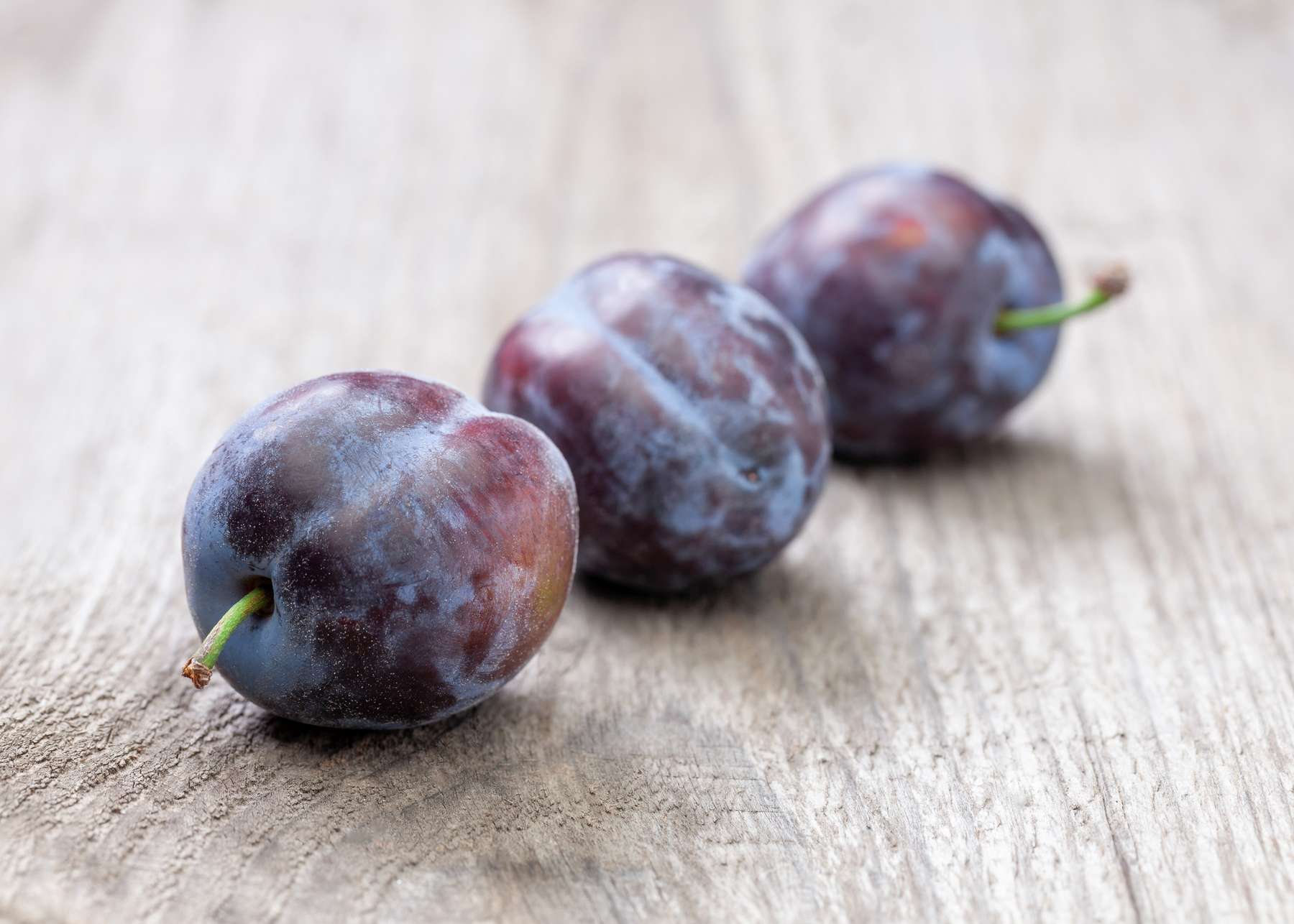 Drei Zwetschken liegen auf einem Holztisch