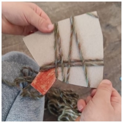 Kind umwickelt Karton-Christbaum mit Wolle